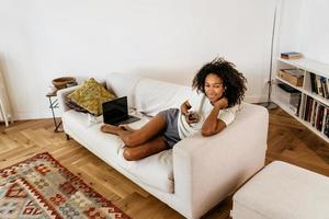 jeune femme noire utilisant un téléphone portable en se reposant sur un canapé