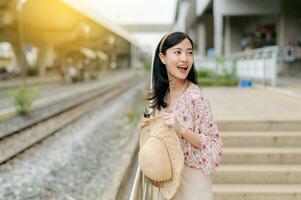 Jeune asiatique femme voyageur avec tissage panier attendre pour train dans train gare. périple voyage mode de vie, monde Voyage explorateur ou Asie été tourisme concept. photo