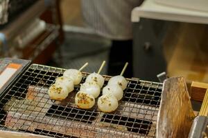 Japonais casse-croûte mitarashi dango fabriqué de riz farine avec une sucré soja sauce glaçage. sur le gril à préparer pour vente à les clients dans le kuromon marché. photo