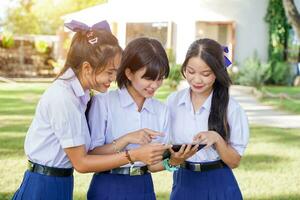 groupe de thaïlandais élèves à la recherche une social réseau sur tablette à école pelouse avec Soleil brillant Contexte. photo