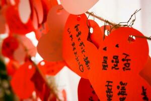 Otaru ville, Japon, 2018 - fermer et surgir Japonais caractères sur souhaitant Mots clés dans rouge papiers et cœur forme pendre sur câble dans letao l'horloge la tour. photo