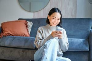 gens et technologie. souriant asiatique femme séance à maison, en utilisant sa mobile téléphone, dactylographie message, sourciller l'Internet ou achats en ligne de téléphone intelligent app photo