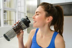 magnifique Jeune sportive les boissons eau, séjours hydraté pendant faire des exercices formation à maison, Faire aptitude des exercices dans vivant pièce photo