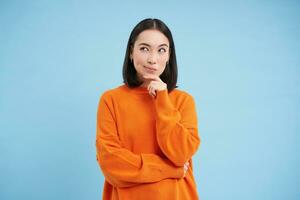 beauté et soins de la peau. proche en haut portrait de content souriant Japonais femme, touche sa clair, embrasé peau, Naturel en bonne santé affronter, permanent plus de bleu Contexte photo