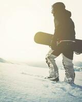 snowboarder marchant avec snowboard au coucher du soleil dans les montagnes enneigées. fond cinématographique de snowboarder freerider solo photo