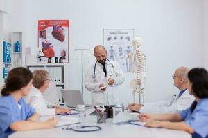 médecin médecin avec stéthoscope discuter OS structure en utilisant Humain squelette en cours d'analyse anatomie corps travail à médical compétence dans conférence réunion chambre. hôpital équipe en présentant traitement photo