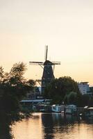 silhouette de le Moulin à vent sur le banques de une canal dans amsterdam, Pays-Bas pendant coucher de soleil, d'or heure. explorant de Hollande photo