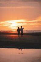 romantique marcher de une Jeune couple sur le des plages de Ostende dans occidental Belgique à le coucher du soleil. l'amour et dévouement. réflexion dans une bassin de l'eau photo