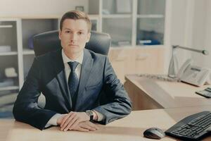 sérieux homme d'affaire assise à une bureau dans une bien éclairé bureau, prêt et prêt pour travail photo