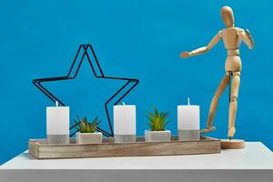 blanc tableau, figurine de humain, vert les plantes dans marmites, Trois gros bougies et un petit dans chandelier dans forme de le fer étoile. bleu Contexte. proche en haut photo