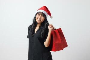 portrait de attrayant asiatique femme avec rouge Père Noël chapeau sentiment content tandis que achat truc. excité fille en portant achats sac. Nouveau année et Noël concept. isolé image sur blanc Contexte photo