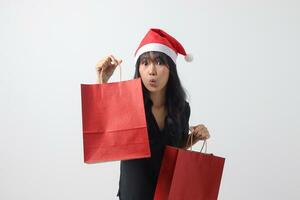 portrait de surpris asiatique femme avec rouge Père Noël chapeau sentiment content tandis que achat truc. excité fille en portant achats sac. Nouveau année et Noël concept. isolé image sur blanc Contexte photo