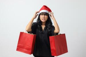 portrait de surpris asiatique femme avec rouge Père Noël chapeau sentiment content tandis que achat truc. excité fille en portant achats sac. Nouveau année et Noël concept. isolé image sur blanc Contexte photo