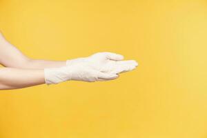 côté vue de Jeune femme mains habillé dans blanc caoutchouc gants en gardant paumes en haut tandis que Aller à laver mains, étant isolé contre Orange Contexte photo