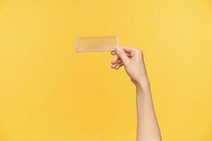 studio photo de Jeune féminin main avec nu manucure en gardant brosse à cheveux horizontalement tandis que posant plus de Orange Contexte. soin des cheveux et Humain mains concept