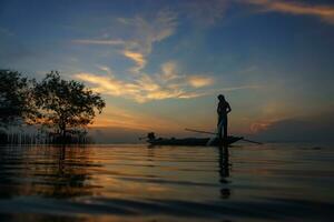 silhouette pêcheur avec le coucher du soleil ciel sur le lac. photo