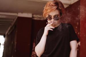 Fille aux cheveux roux courts et lunettes de soleil miroir fumant une cigarette photo