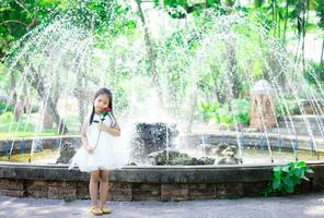 mignonne peu asiatique fille dans blanc robe en portant une rouge Rose dans le parc photo