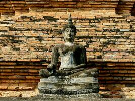 une Bouddha statue est séance sur Haut de une brique mur photo