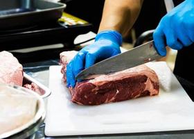 le chef coupe la viande crue avec un couteau sur une planche, le cuisinier coupe la viande crue