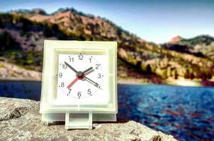 une petit l'horloge séance sur une Roche près une Lac photo