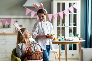 Une fille et un garçon souriants font un panier de Pâques à la maison dans la cuisine photo