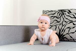 portrait de une bébé fille avec une bandage et une arc sur sa tête sur une canapé photo