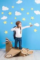 peu rêveur fille en jouant avec une papier carton avion à le studio avec bleu ciel et blanc des nuages Contexte. photo