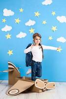 peu rêveur fille en jouant avec une papier carton avion à le studio avec bleu ciel et blanc des nuages Contexte. photo