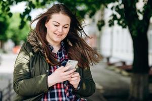 souriante, jolie fille regardant quelque chose au téléphone, à l'extérieur photo