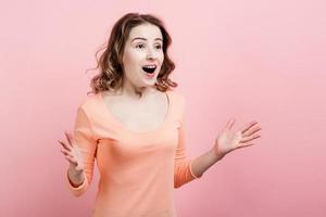 une belle fille agréablement surprise a ouvert ses bras contre un mur rose photo