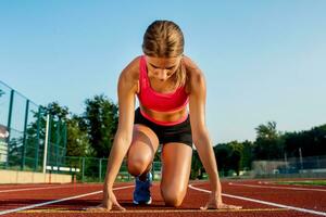 Jeune femme athlète à départ position prêt à début une course sur piste de course. photo