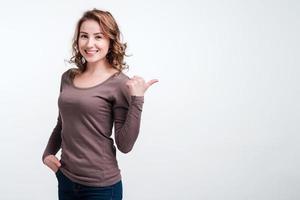 jeune fille souriante montre le doigt sur le côté. fond blanc, gros plan. photo