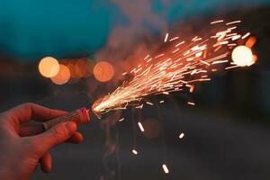 Jeune homme éclairage en haut pétard dans le sien main en plein air dans soir. gars avoir prêt pour Nouveau année amusement avec feux d'artifice ou pyrotechnique des produits fermer coup photo