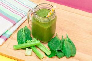 Frais vert smoothie de pomme, céleri, et épinard dans verre smoothie pot avec Jaune cocktail paille sur en bois Coupe planche. végétalien désintoxication boire. végétarien culture. en bonne santé en mangeant et fruit régime photo