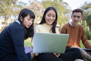 groupe d'étudiants universitaires asiatiques assis sur l'herbe verte travaillant et lisant dehors ensemble dans un parc