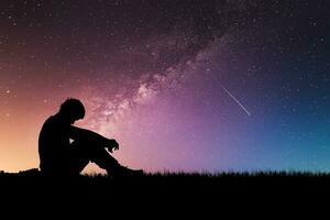 concept de solitude, de désespoir et de regret. homme solitaire dans le pré sur fond d'étoiles et de voie lactée. photo