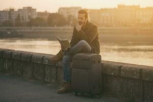 confus homme d'affaire avec valise et ville carte séance perdu par le rivière.tonique image photo