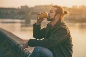 Beau moderne homme d'affaire jouit en buvant café et repos par le rivière.tonique image. photo