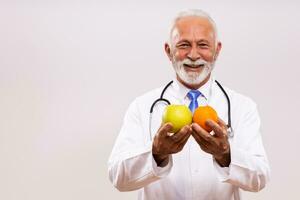 portrait de Sénior médecin en portant des fruits sur gris Contexte. photo