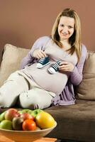 souriant Enceinte femme séance sur canapé et en portant bébé chaussons photo