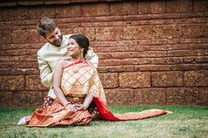 la mariée asiatique et le marié caucasien passent un moment romantique avec une robe thaïlandaise photo