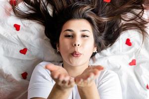 Jeune femme brune heureuse allongée dans le lit en soufflant un baiser photo