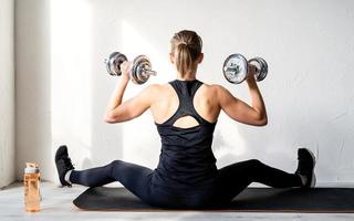 Vue arrière de la jeune femme blonde travaillant avec des haltères montrant ses muscles du dos et des bras photo