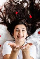 Jeune femme brune heureuse allongée dans le lit en soufflant un baiser photo