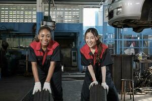 deux diverse femelle automobile mécanicien ouvrier les partenaires rivaliser à pousser voiture roues pour changement et réparation à garage, véhicule entretien un service emplois, industrie profession, et professionnel la main d'oeuvre travaux. photo