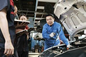 asiatique Masculin professionnel automobile ingénieur superviseur décrit voiture moteur entretien et réparation travail avec mécanicien ouvrier états-majors équipe dans réparer un service garage, spécialiste métiers dans auto industrie. photo