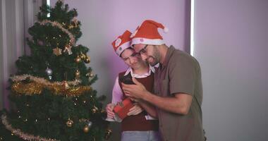 portrait de Jeune couple prise selfie et souriant tandis que permanent avec décoré Noël arbre dans le arrière-plan, célébrer Noël et Nouveau année, les amoureux avoir moment romantique et content ensemble. photo