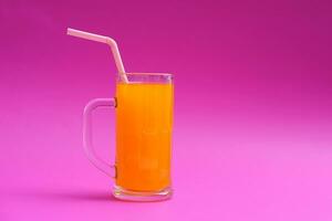 verre agresser de Orange jus avec en buvant paille. rose Contexte. concept, Matin rafraîchissant boisson. doux, grincheux et haute vitamine c. photo