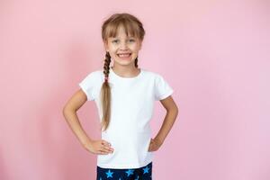 magnifique peu blond fille avec longue cheveux dans blanc T-shirt souriant sur une rose Contexte photo